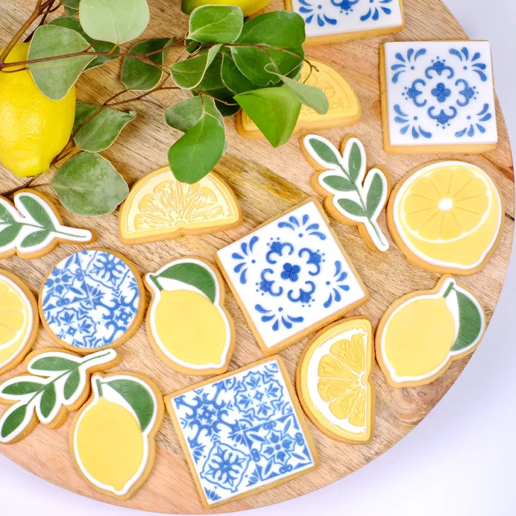 Mehrere gelbe, weiße und blaue Kekse mit Zitronen und Fliesenmotiven auf einer runden Holzplatte.
