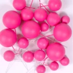 Mehrere pinke Kugeln aus Kunststoff auf Drähten in verschiedenen Größen vor weißem Hintergrund.