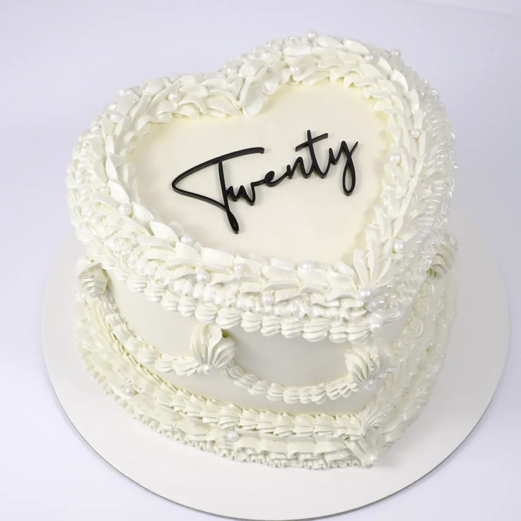 Eine weiße Torte in Herzform mit einem Aufleger aus schwarzem Acryl "Twenty".