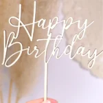 Ein Cake Topper aus Holz mit der Aufschrift "Happy Birthday", der von einer Frauenhand hochgehalten wird.