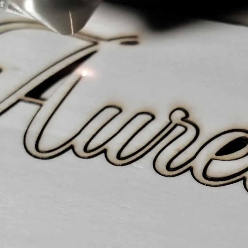 Nahaufnahme einer Holzplatte, in die mit einem Laser ein Schriftzug eingraviert wird.