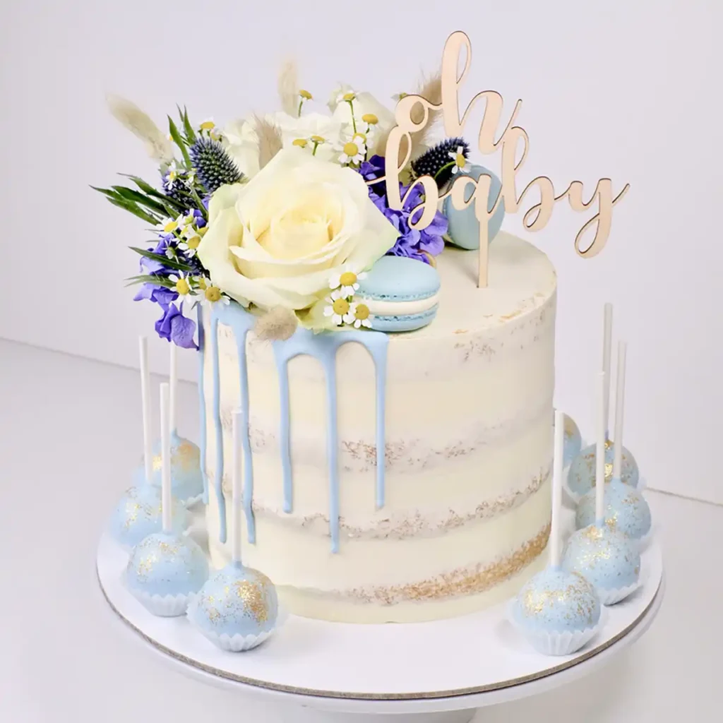 Ein Cake Topper aus Holz mit dem Schriftzug "oh baby" auf einer weiß-hellblauen Torte.