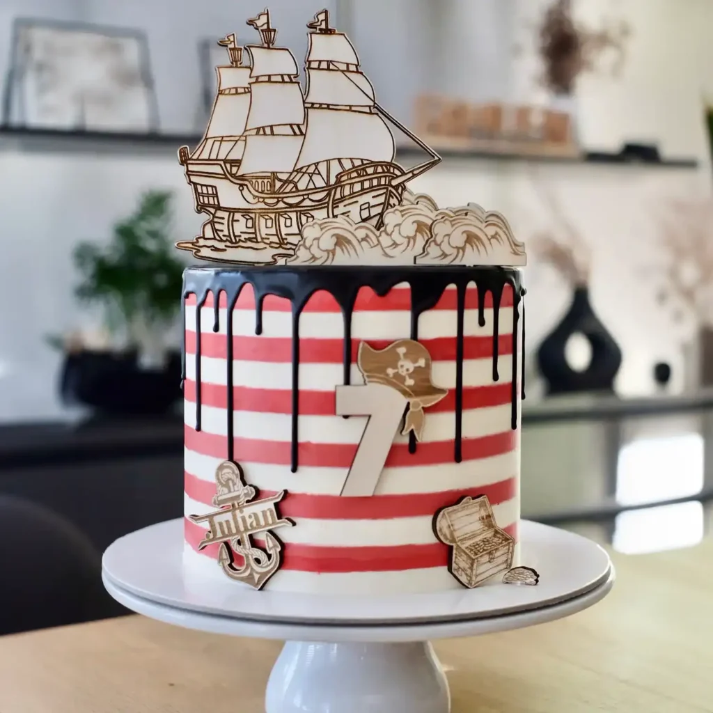 Eine weiß-rote Torte mit Cake Toppern aus Holz mit einem Schiff und Piratenmotiven.