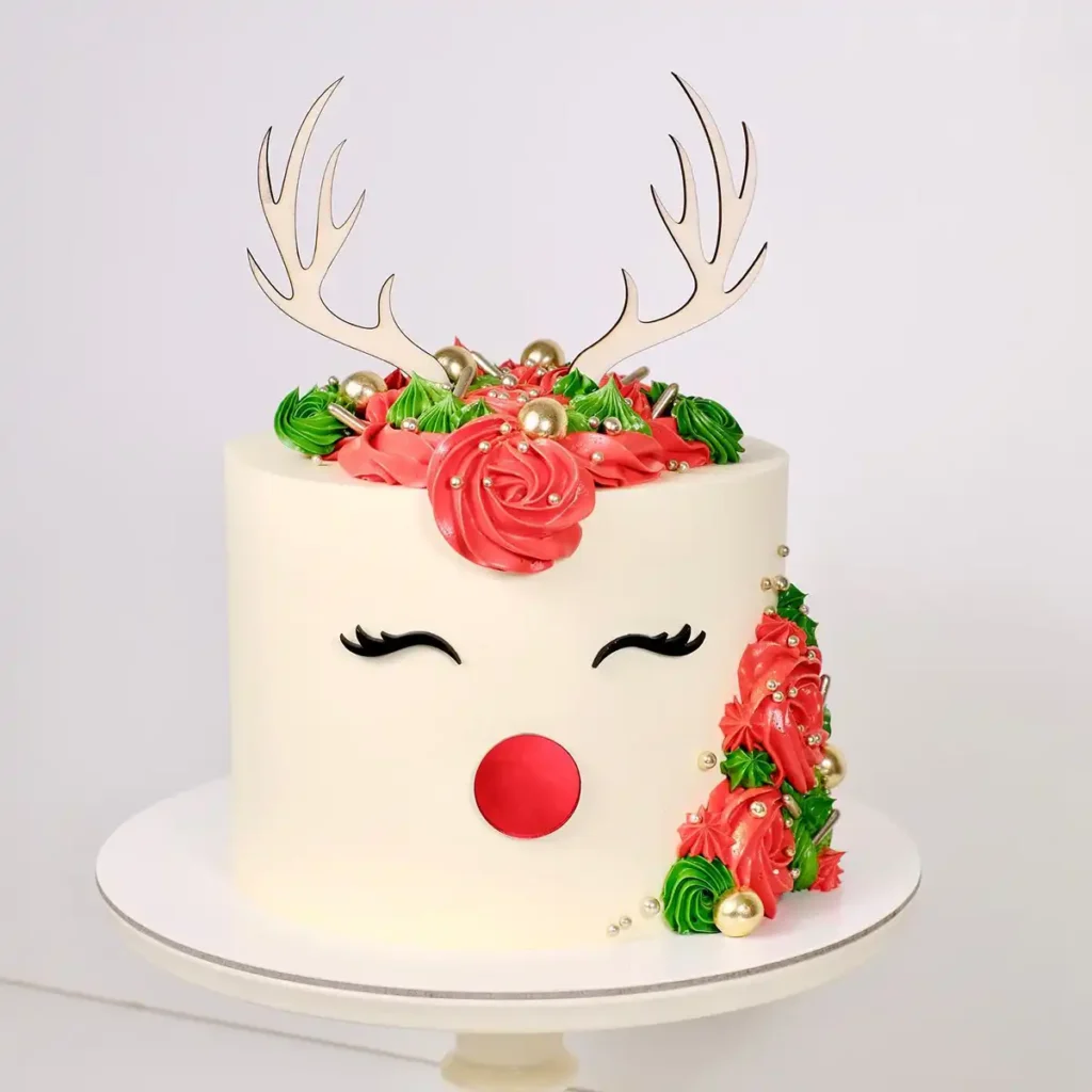 Eine weiße Torte mit einem Rentier Gesicht als Cake Topper und rot-grüner Creme.