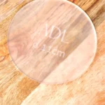 Eine matt transparente Ganache Platte mit der Gravierung "ADL⌀ 11cm" auf einem Holztisch.