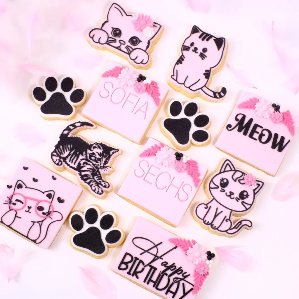 Zwölf rosane Kekse mit verschiedenen Katzenmotiven auf einem rosanen Hintergrund.
