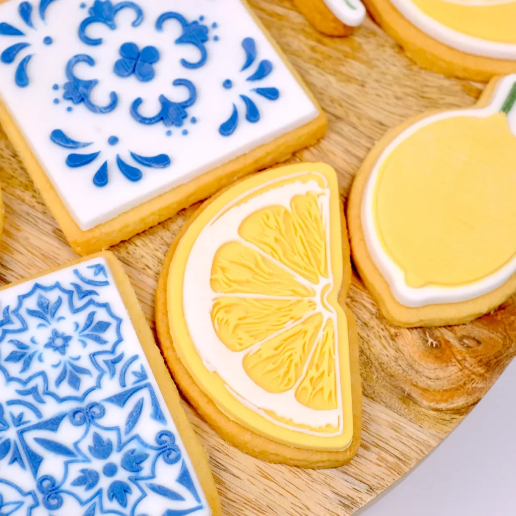 Vier Kekse mit Zitronen- und Fliesenmustermotiv auf einer Holzplatte.