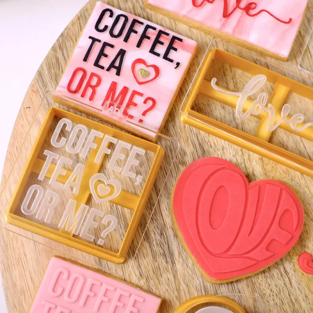 Mehrere rosane und rote Kekse mit Keksstempeln und Ausstechern mit Motiven zum Thema Valentinstag.