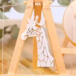 Ein transparenter Keksstempel mit gravierter Giraffe auf einer kleinen Staffelei aus Holz.