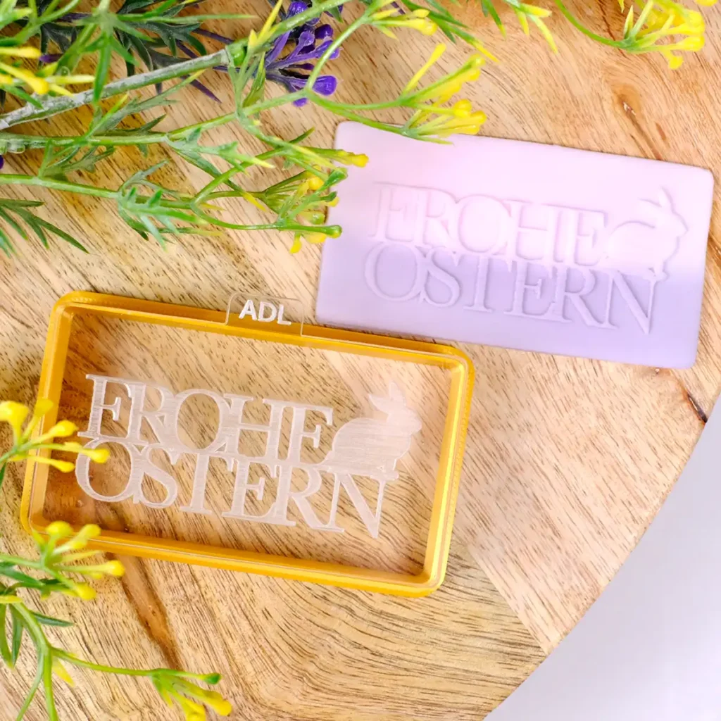 Ein rechteckiger, lilaner Keks mit Schriftzug "Frohe Ostern" und passendem Keksstempel und Ausstecher.