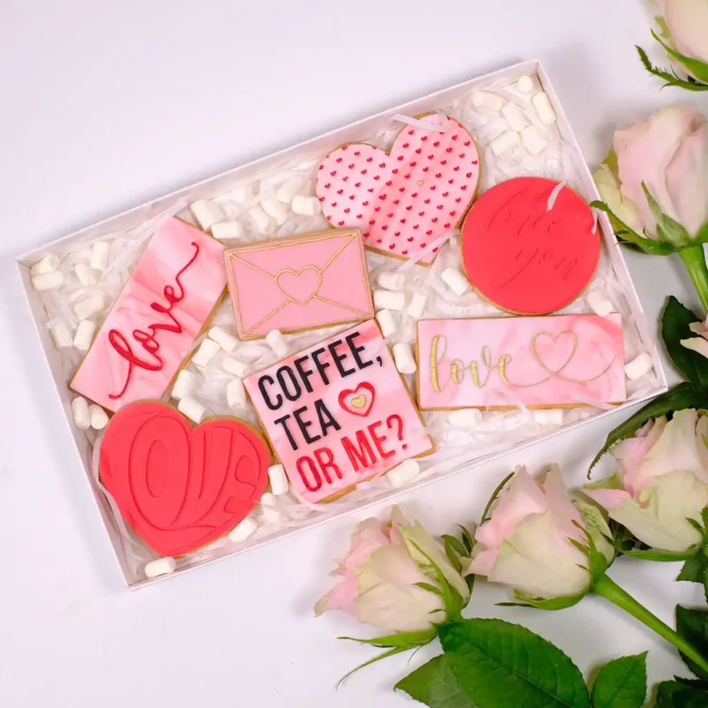 Eine weiße Box mit sieben rosanen und roaten Keksen mit Motiven zum Valentinstag.